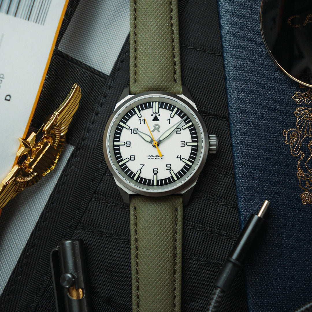Watch with a white face and green strap on a surface with travel documents and a pen.
