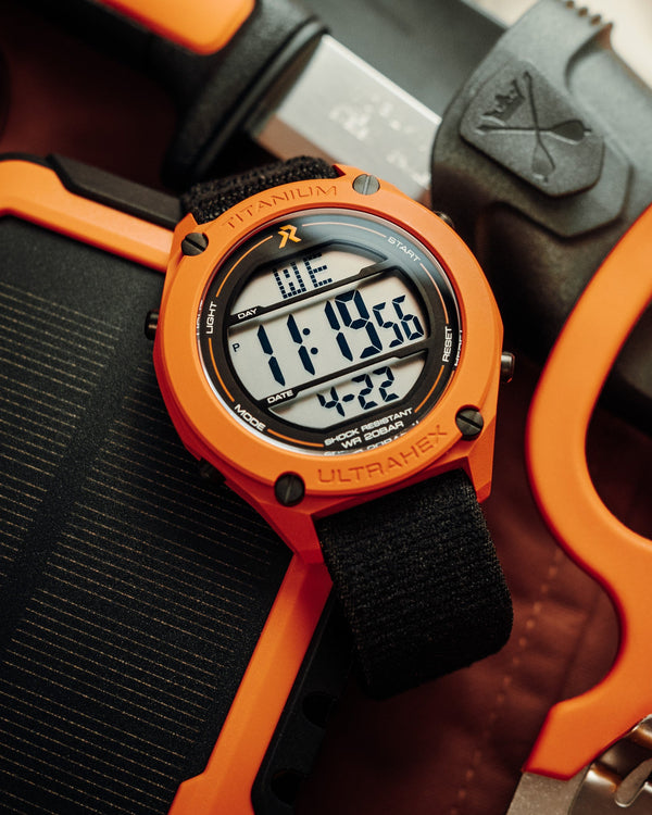 Orange digital watch with black strap on a background of tools
